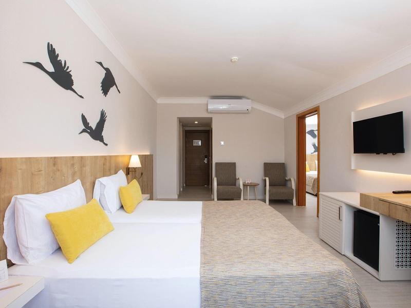 Camera d'albergo moderna con due letti, cuscini gialli, decorazioni murali e TV a schermo piatto.