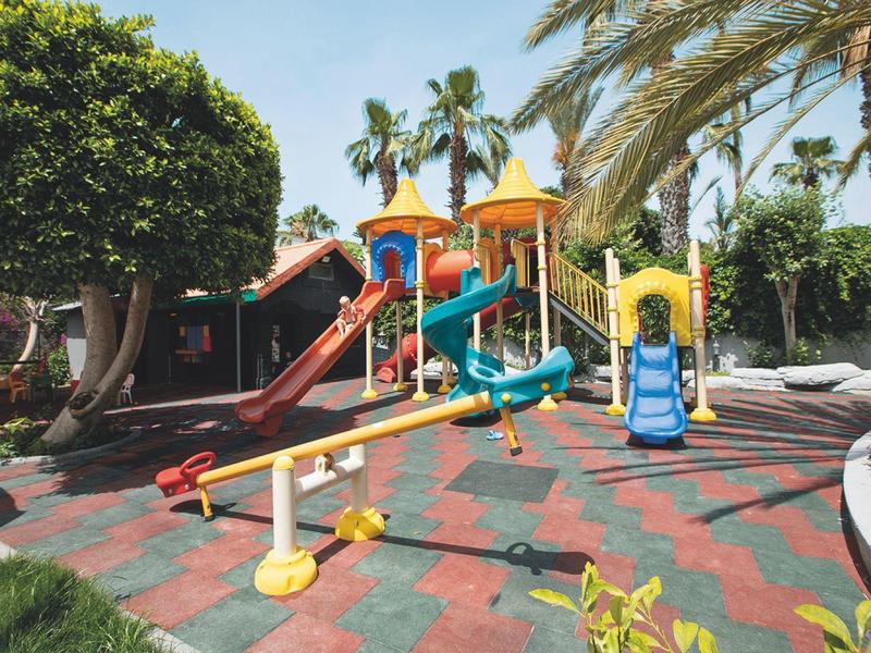 Parco giochi colorato per bambini con scivoli e altalene in un giardino tropicale.