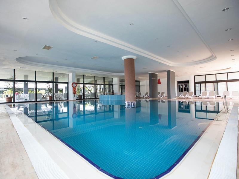 Grande piscina coperta riscaldata con pareti bianche e grandi finestre in un hotel