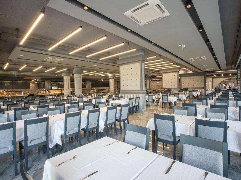 Ampia sala da pranzo moderna con molti tavoli e sedie, illuminazione luminosa.