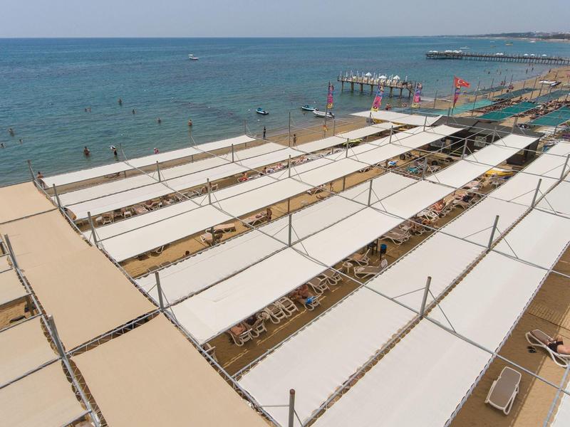 Aree prendisole coperte sulla spiaggia con vista sul mare e bagnanti.