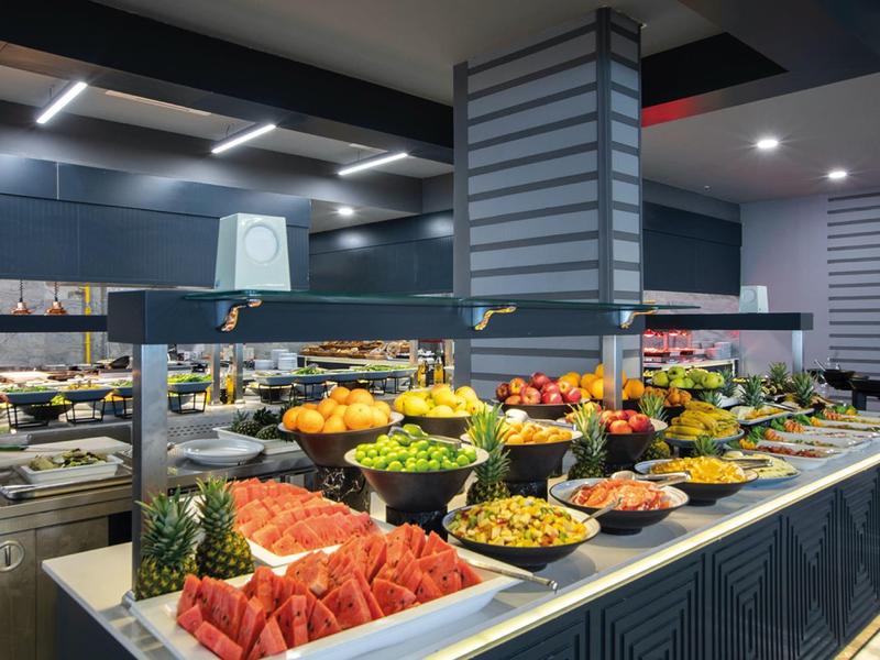 Buffet di frutta colorata con meloni, ananas e uva in un ristorante moderno.