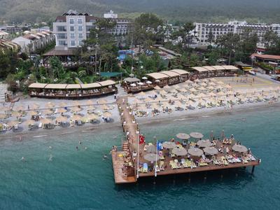 Strand mit Holzsteg, Liegestühlen, Sonnenschirmen und Hotels im Hintergrund.