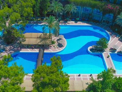 Grande piscina dell'hotel di forma organica, circondata da alberi verdi e lettini.