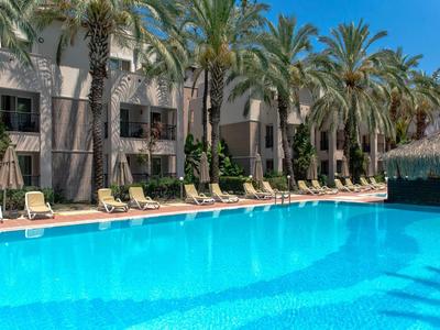 Grande piscina davanti a un hotel con palme e lettini sotto un cielo blu.