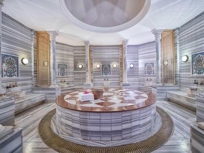 Grande hammam turca di lusso con pareti in marmo e tavolo centrale in pietra riscaldato.