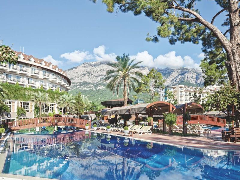 Piscina dell'hotel con sdraio, palme e montagne sullo sfondo in una giornata di sole.