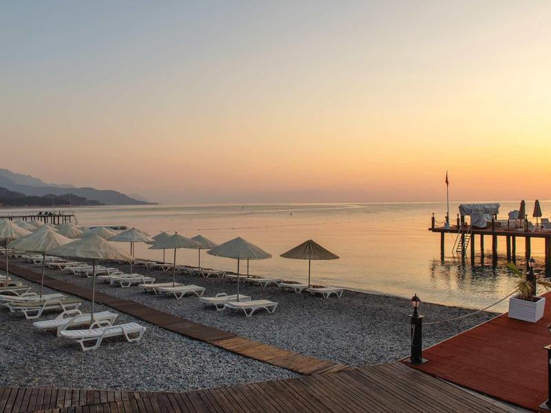 Alba su una spiaggia tranquilla con lettini e un molo che si estende nel mare.