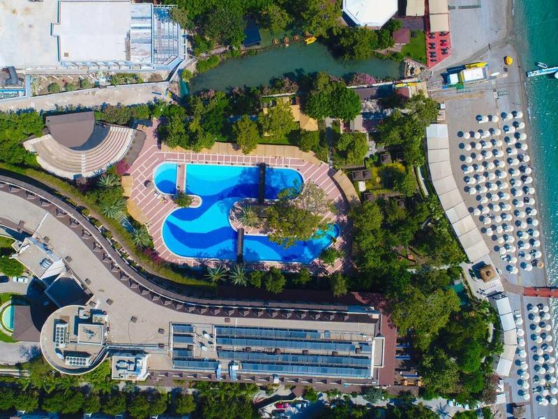 Vista aerea di un resort con piscina, spiaggia e lettini vicino al mare.