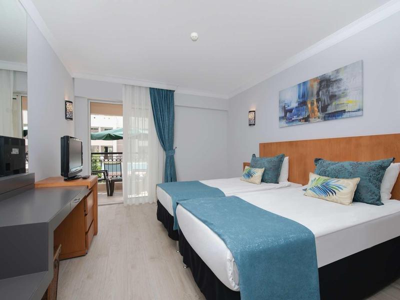 Camera d'hotel moderna con letto matrimoniale, scrivania, TV e balcone con tende.