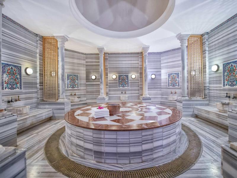 Grande hammam turca di lusso con pareti in marmo e tavolo centrale in pietra riscaldato.