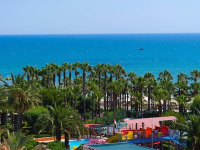 Landschaft mit grünem Palmengarten, bunten Wasserrutschen und blauem Meer im Hintergrund.