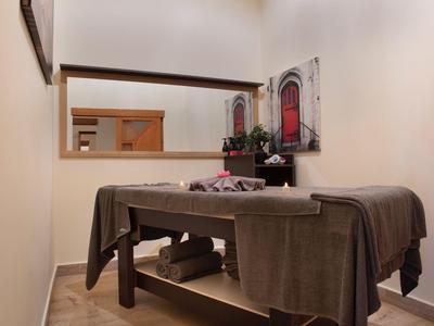 Behandlungsraum mit Massagebank, braunen Decken, Spiegel und Bild mit roter Tür an heller Wand.