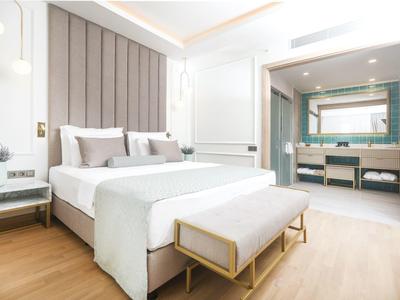 Helles Schlafzimmer mit großem Bett, grauen Akzenten und verbundenem Badezimmer mit Doppelwaschbecken.