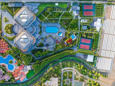 Luftaufnahme eines Resorts am Strand mit Pools, Tennisplätzen, Gartenanlagen und schmalem Sandstrand.
