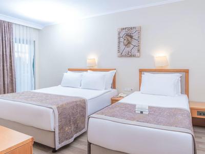 Helles Hotelzimmer mit zwei Betten, Nachttischen, Lampen und einem Wandbild über den Betten.