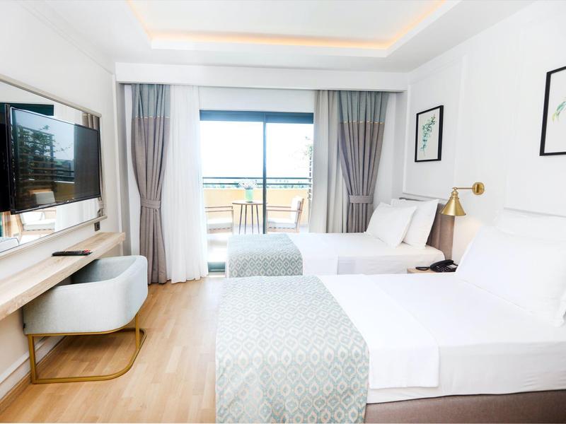 Camera d'hotel luminosa con letto matrimoniale, TV, scrivania e vista sulla terrazza.