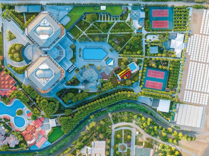 Vista aerea di un resort con piscina, campi da tennis, giardini e spiaggia