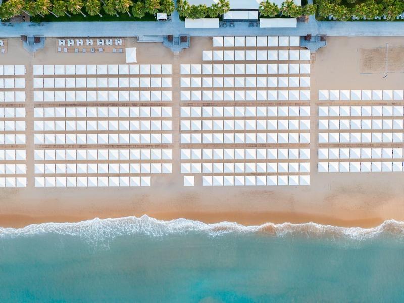 Vista aerea di una spiaggia con lettini e ombrelloni ordinati vicino al mare.