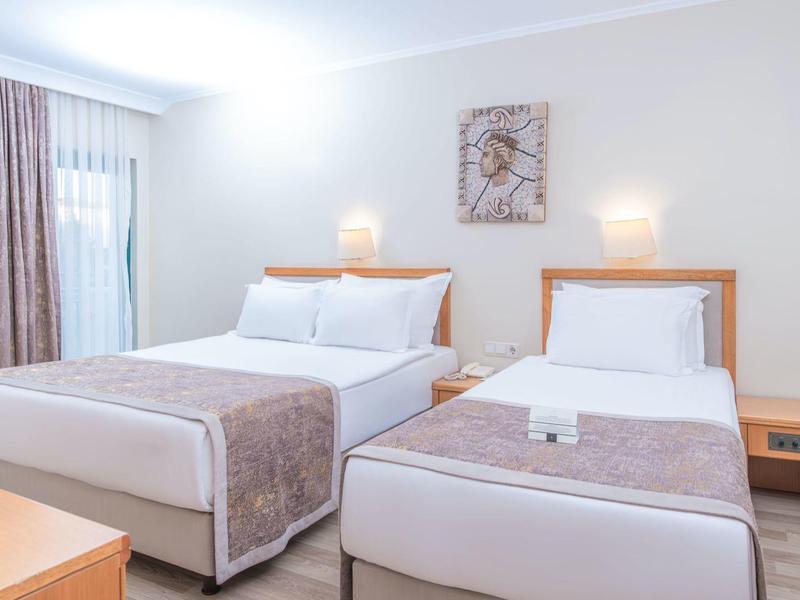 Camera d'hotel luminosa con due letti, comodino e illuminazione soffusa.