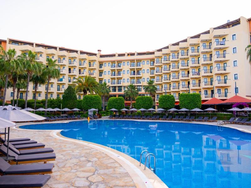 Hotel con grande piscina all'aperto, lettini e palme in una giornata di sole