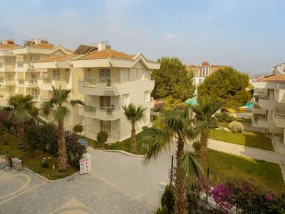 Complesso residenziale moderno con edifici multipiano, palme e aree verdi curate sotto un cielo azzurro.