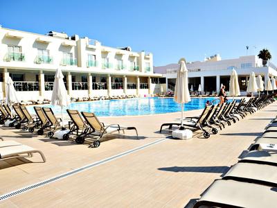 Hotelová oblast bazénu s lehátky a bílými slunečníky za slunečného počasí.