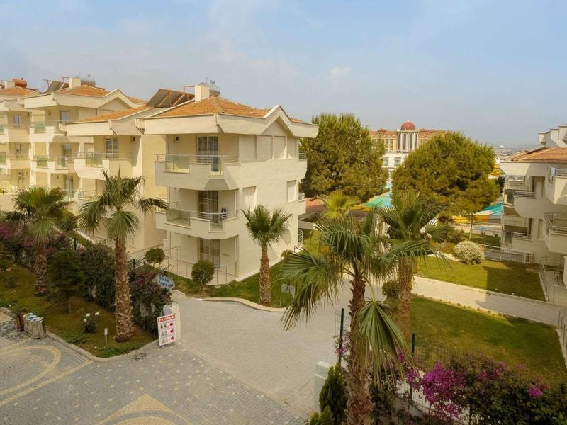 Complesso residenziale moderno con edifici multipiano, palme e aree verdi curate sotto un cielo azzurro.