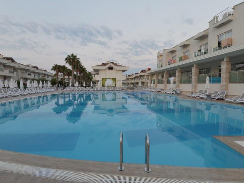 Grande piscina all'aperto con lettini presso complesso alberghiero sotto cielo nuvoloso.