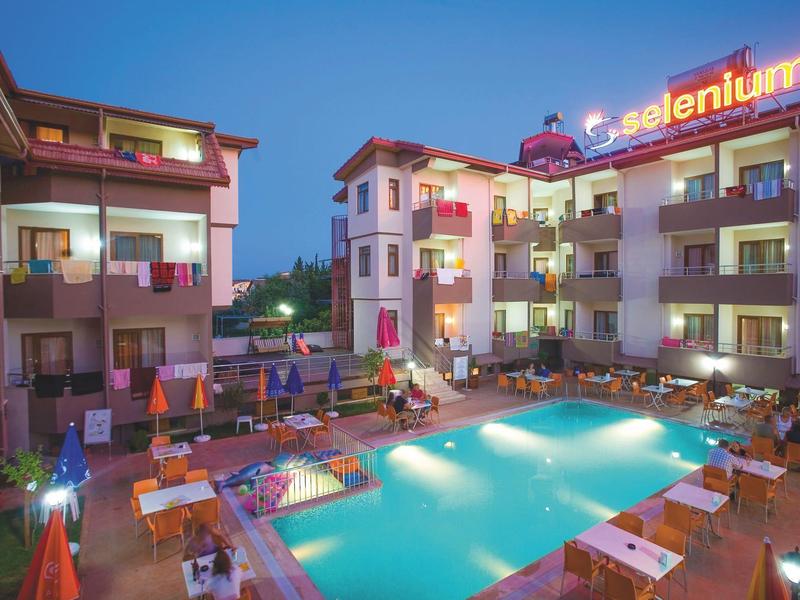 Beleuchtetes Hotel mit Pool und Sonnenliegen am Abend unter klarem Himmel.