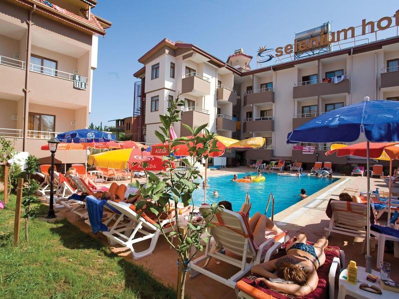 Hotelpool mit Gästen auf Liegestühlen und bunten Sonnenschirmen an einem sonnigen Tag.