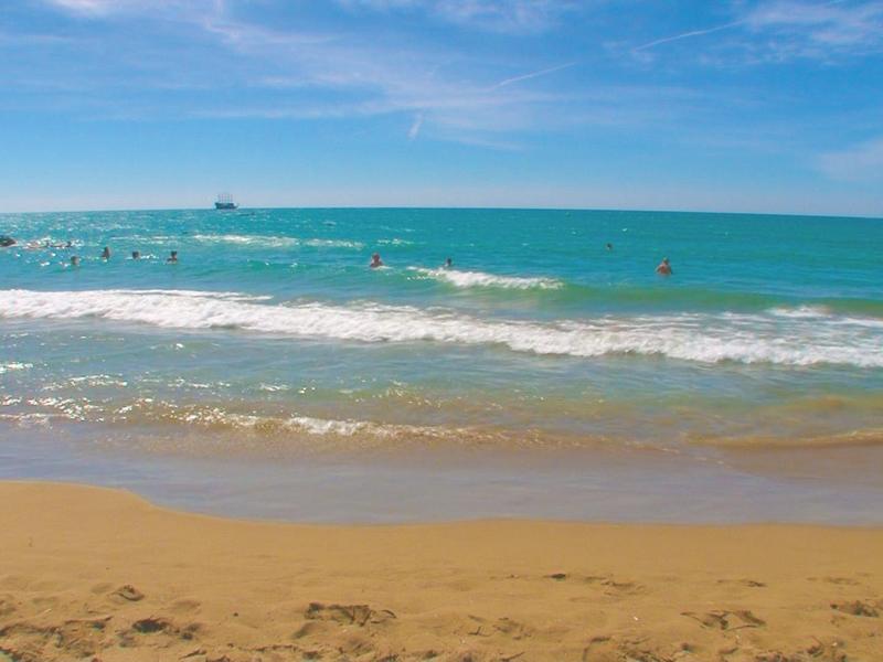 Strand mit goldfarbenem Sand und ruhigem Meer unter blauem Himmel.