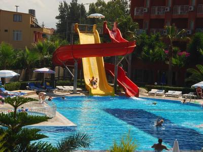 Ein Schwimmbecken mit mehreren bunten Wasserrutschen und Liegestühlen in sonniger Umgebung.