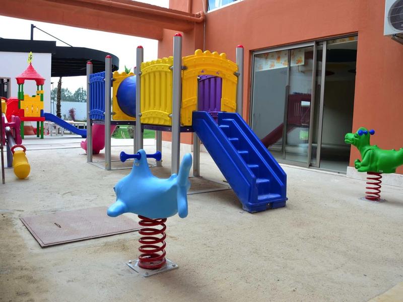 Area giochi colorata per bambini con scivoli e giochi a molla in un cortile interno.