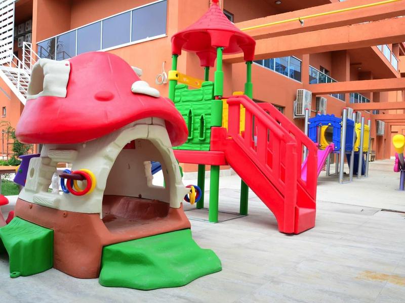 Area giochi colorata per bambini con casa fungo e scivoli in un cortile di un hotel.