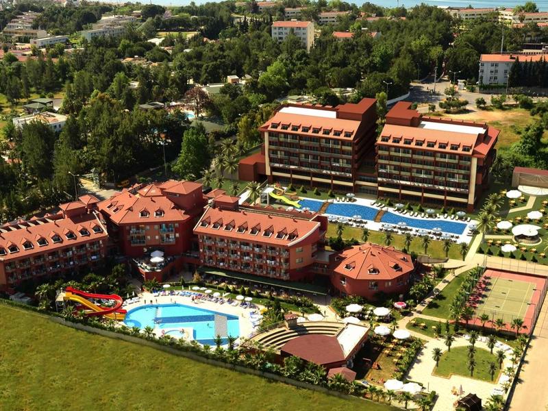 Grande resort alberghiero con più edifici, piscine e campi da tennis in un ambiente verde.