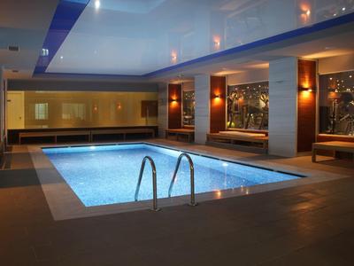 Innenbereich mit beleuchtetem rechteckigem Schwimmbecken, Holzbank, warmem Licht und Glasfenstern.