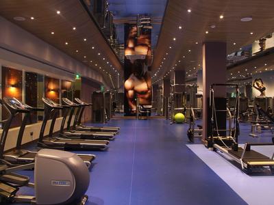 Moderner Fitnessraum mit blauen Boden, Laufbändern, Gewichten und gedämpfter Beleuchtung.