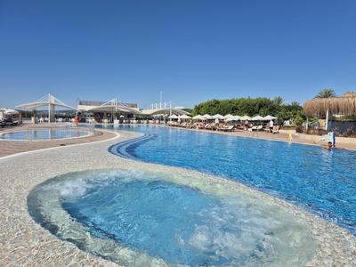 Großer Hotelpool mit integriertem Whirlpool, Liegestühlen und klarem blauem Himmel im Hintergrund.