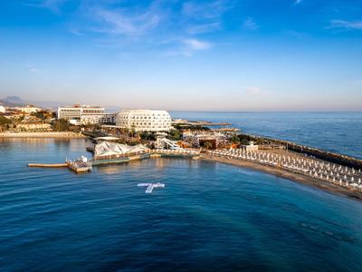 Hôtel de luxe en bord de mer avec piscine, plage et eau bleue claire sous un ciel dégagé.