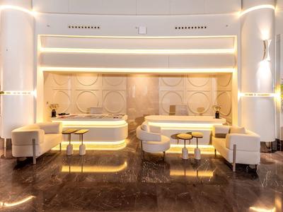 Hall d'hôtel moderne avec sièges blancs, éclairage doré et sol brillant.
