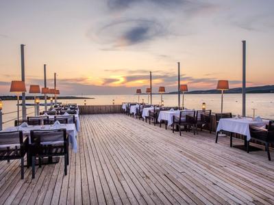Terrasse en bois avec tables et chaises dressées au coucher du soleil près de l'eau.
