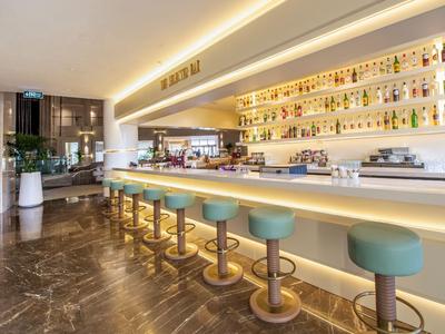 Espace bar d'hôtel moderne avec comptoir éclairé et tabourets turquoises.