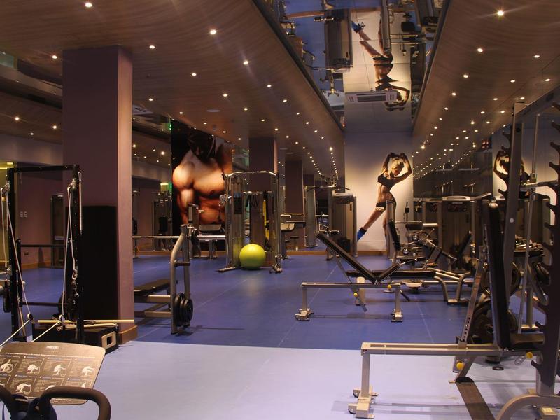 Salle de sport moderne avec équipements variés, sol bleu et éclairage chaud.