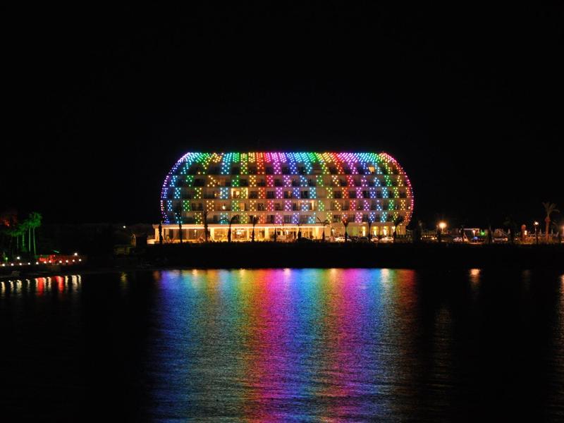 Hôtel moderne illuminé multicolore, reflet vibrant sur l'eau de nuit.