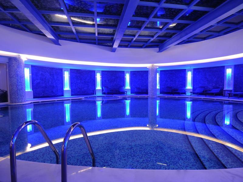 Piscine intérieure éclairée en bleu avec des marches en pierre et un plafond structuré.