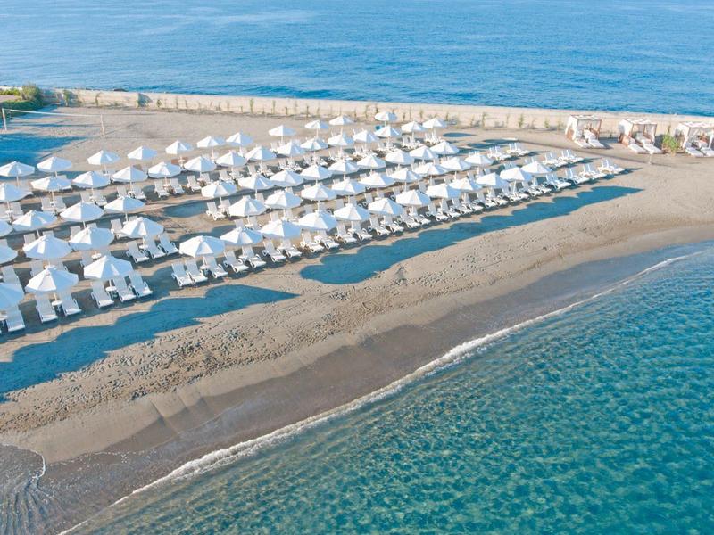 Plage avec rangées de parasols blancs près de l'eau turquoise claire.