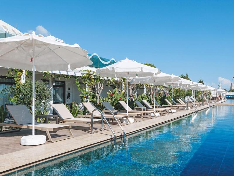 Piscine extérieure avec chaises longues et parasols sous un ciel bleu clair.