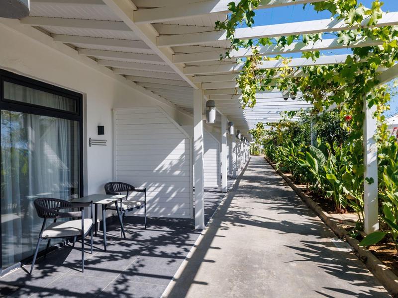 Allée ombragée avec pergola et tables devant les chambres d'un hôtel.