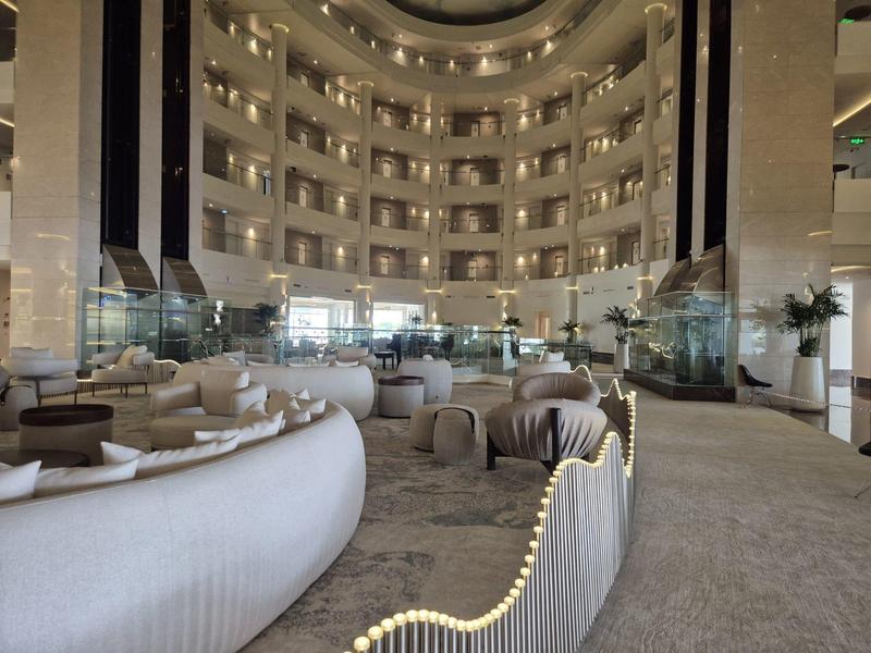 Grand hall d'hôtel avec sièges élégants et balustrades éclairées sous une grande verrière.